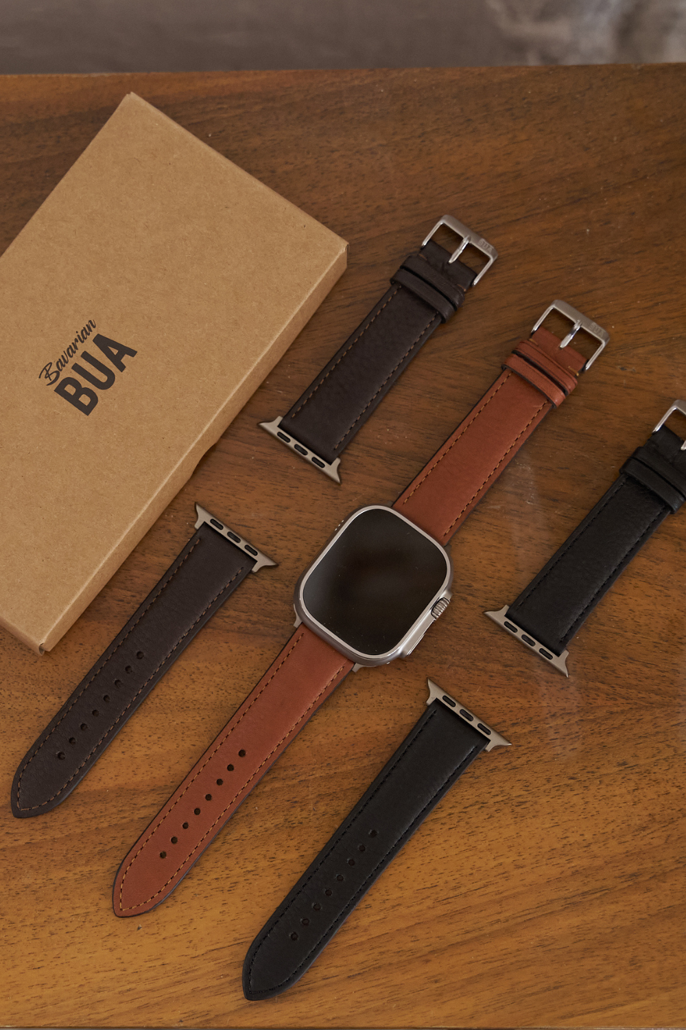 Apple Watch Ultra mit unseren 2 Lederarmbändern, dargestellt auf einem Holztisch.