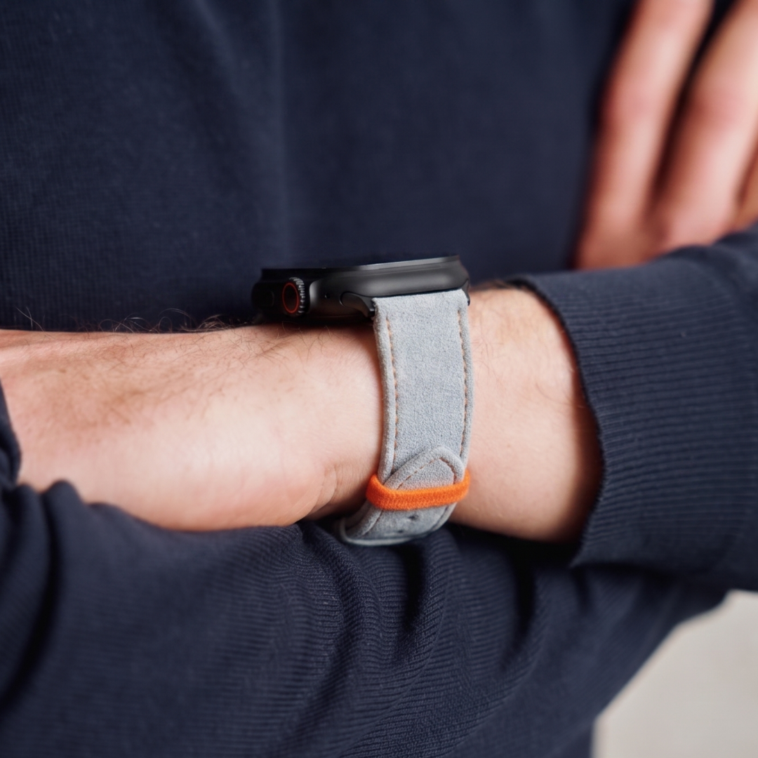Hellgraues Alcantara Armband mit orangenen Ziernähten für Apple Watch Ultra am Handgelenk getragen