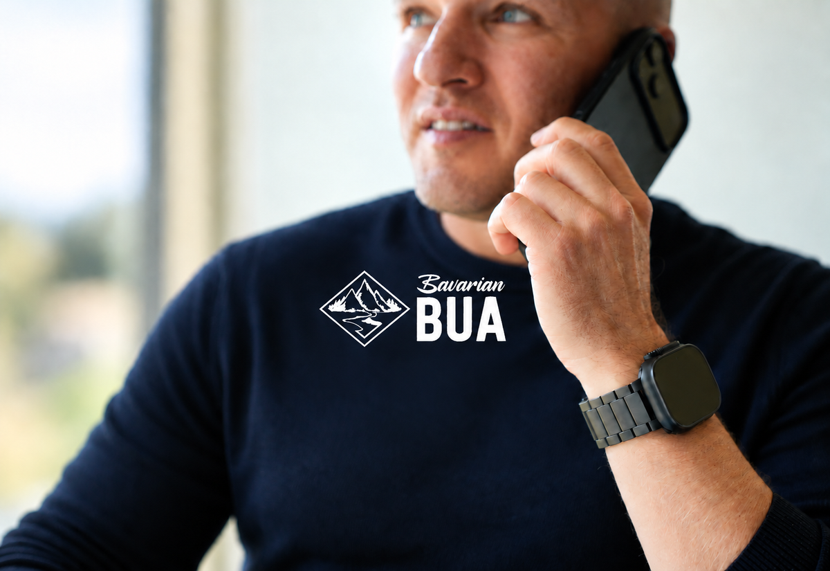 Michael trägt beim Telefonieren ein dunkles Titan-Gliederarmband; weißes Bavarian-BUA-Logo mittig